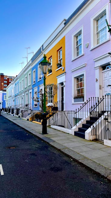 A row of colourful Victorian-style terraced houses on a narrow street in Notting Hill, London, with facades painted in shades of blue, pink, and white. The image captures the architectural details suc